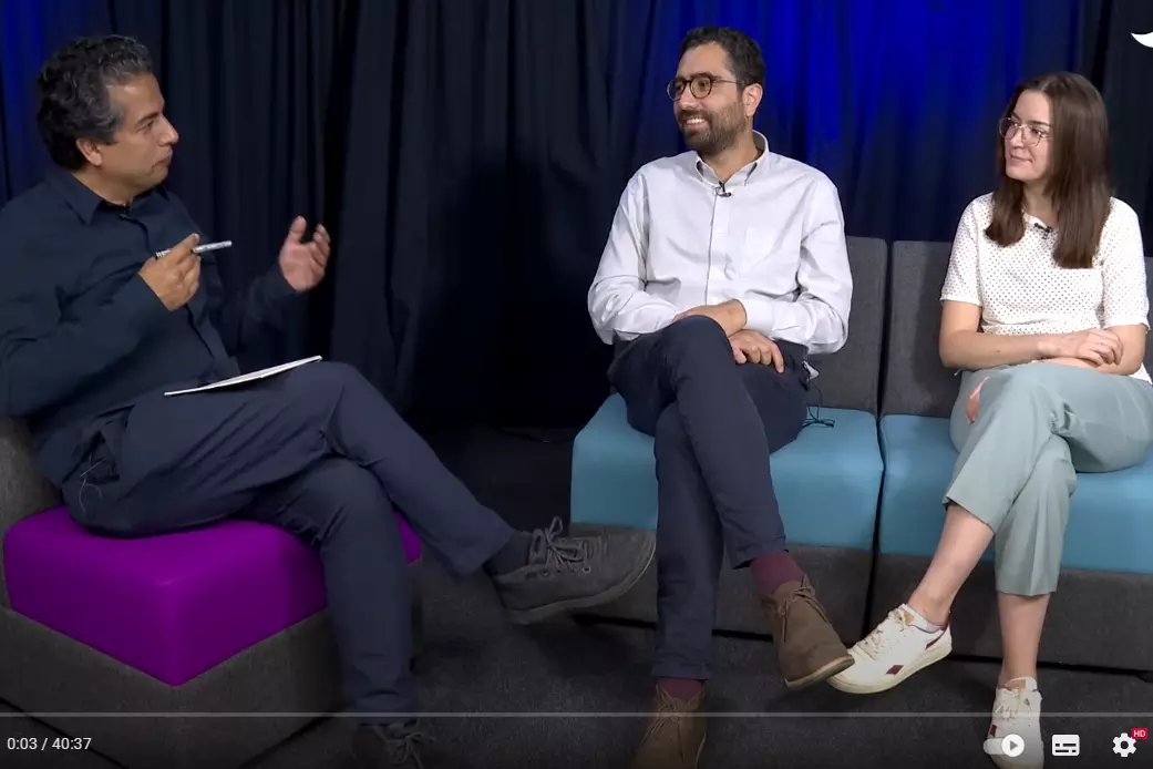 an interviewer on a purple chair taliking to jose maria and another woman seated on a sofa